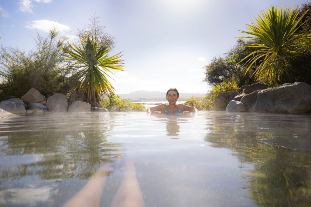 Une femme qui se baigne au Polynesian Spa, à Rotorua. Des montagnes et arbres exotiques en arrière plan
